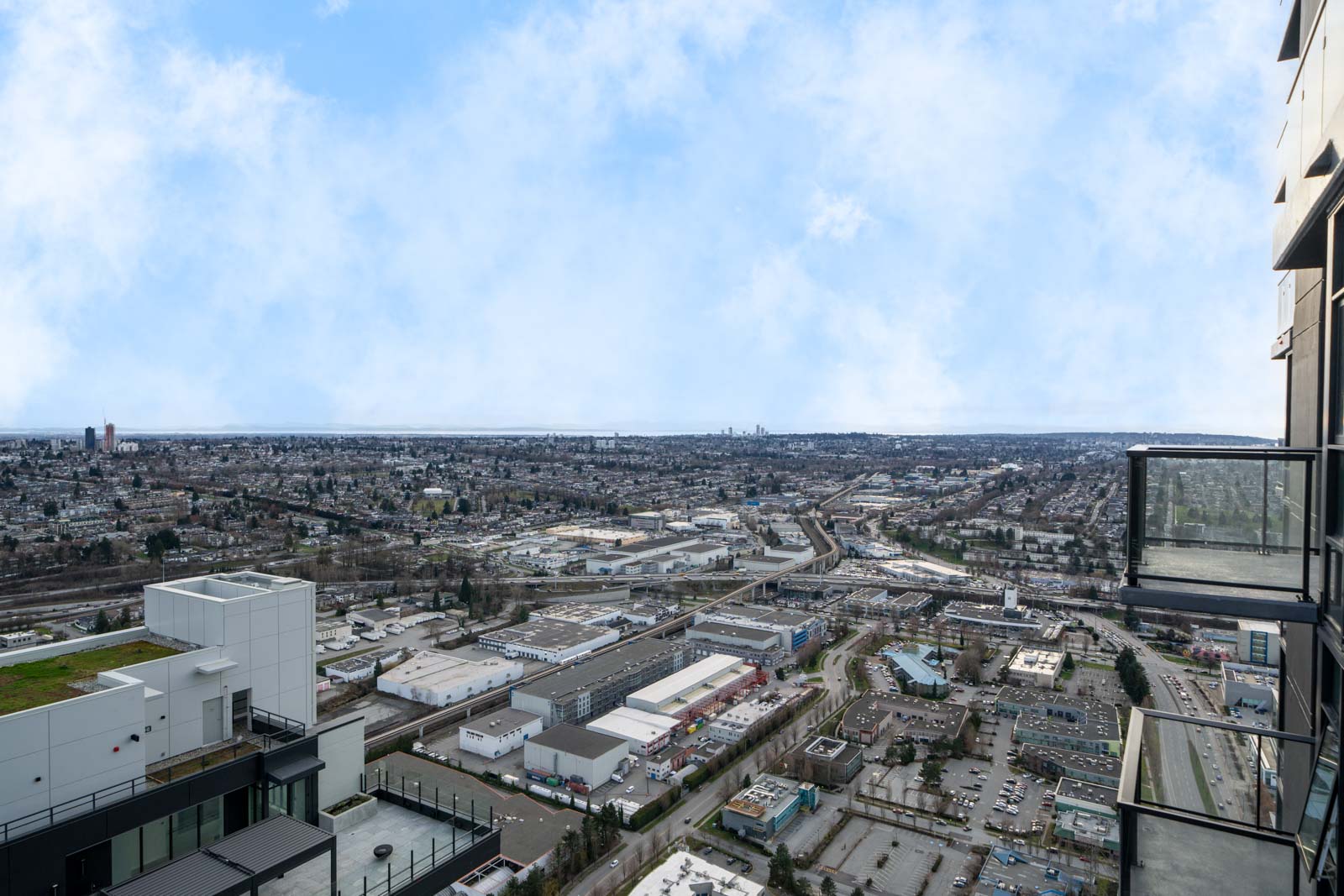 Aerial view of an urban landscape with roads, industrial buildings, and residential areas under a cloudy sky, seen from a high-rise balcony.