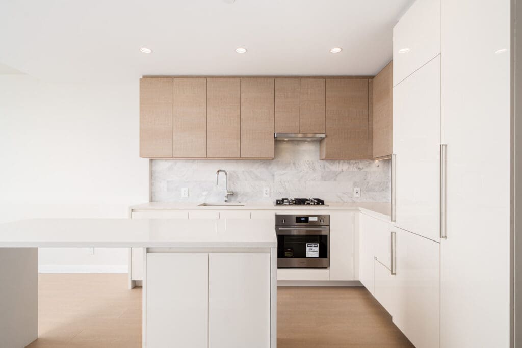 Modern kitchen with white countertops, wooden cabinets, and stainless steel appliances, including a gas stove and oven. Bright lighting and a minimalist design.