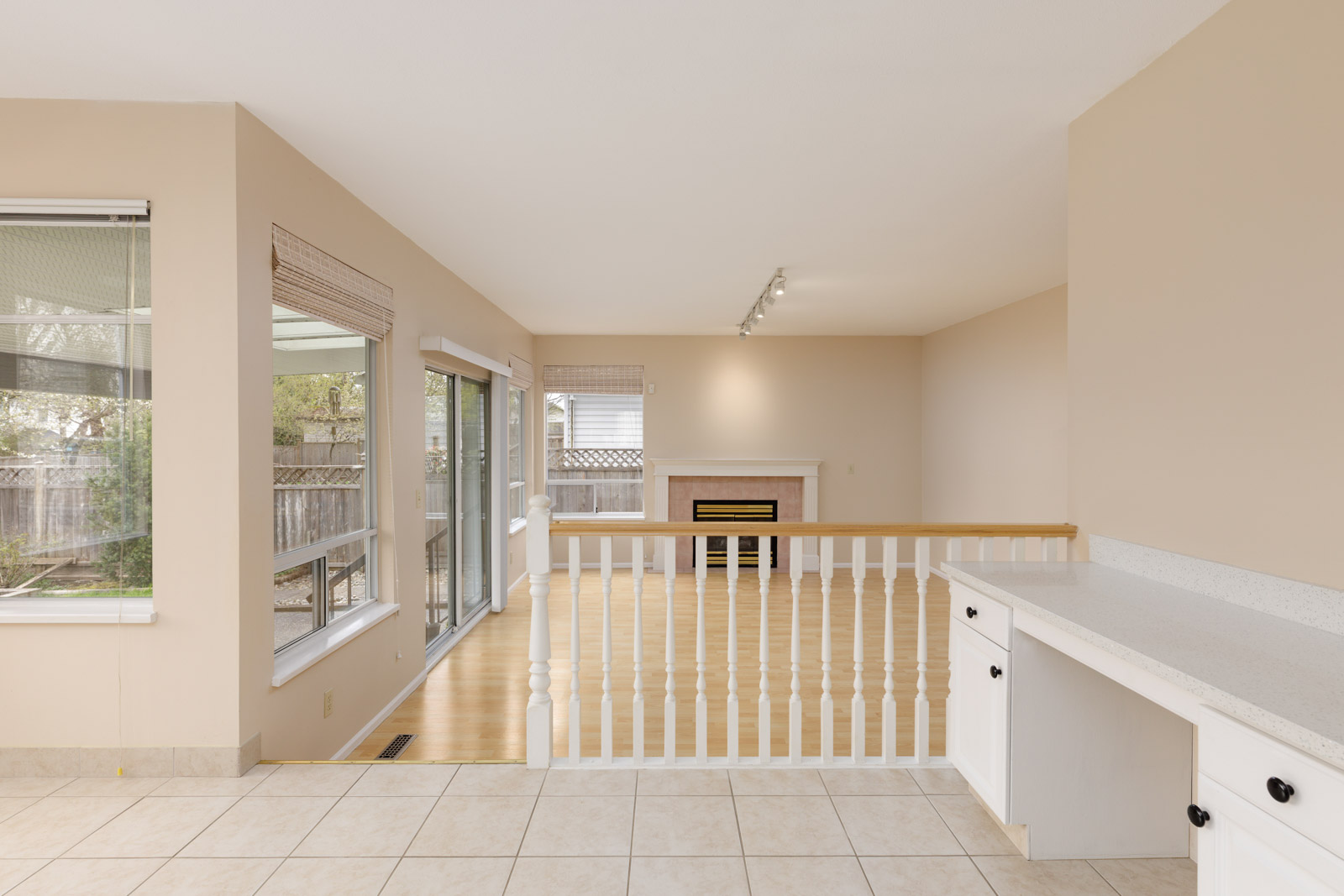 Open-plan room with tile and wood flooring, white railings, large windows, sliding glass door, and a fireplace. Neutral wall colors and natural light create a bright atmosphere.
