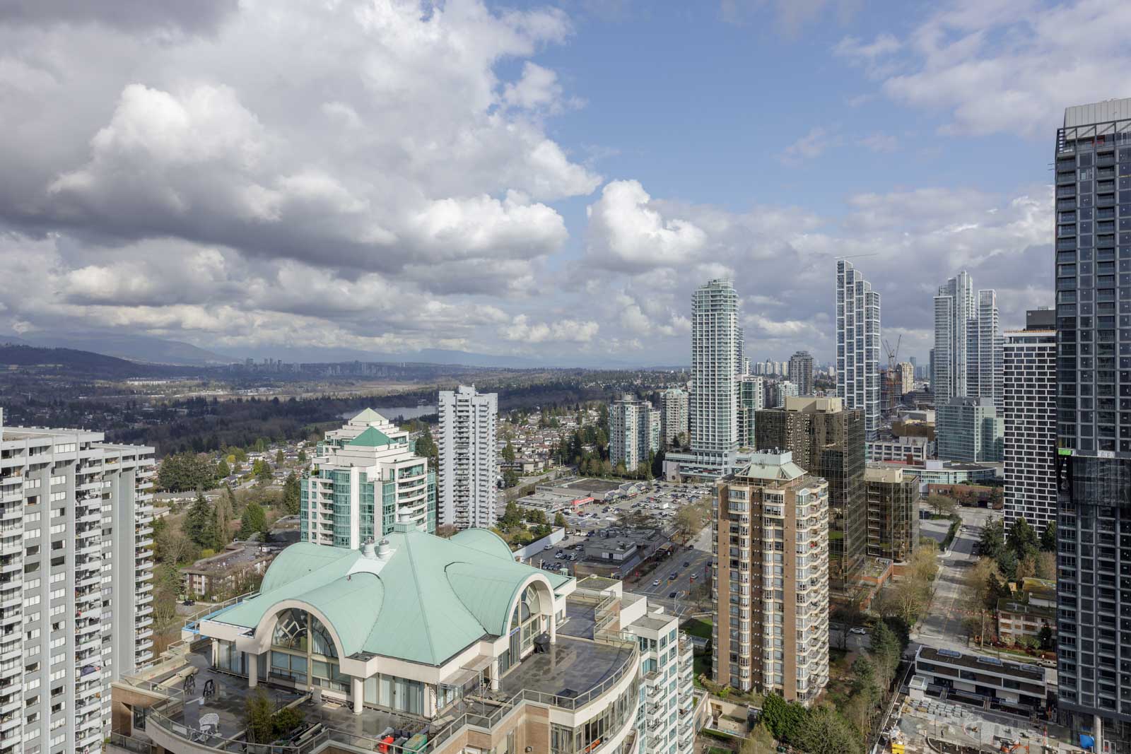 A cityscape view of high-rise buildings with a distinctive white-roofed structure in the foreground under a partly cloudy sky.