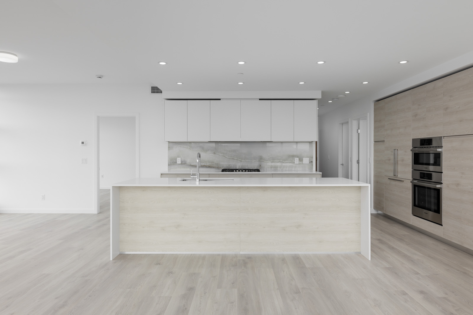Modern kitchen with white cabinetry, a central island, and stainless steel appliances. Light wood flooring and recessed lighting add a sleek, minimalist touch.