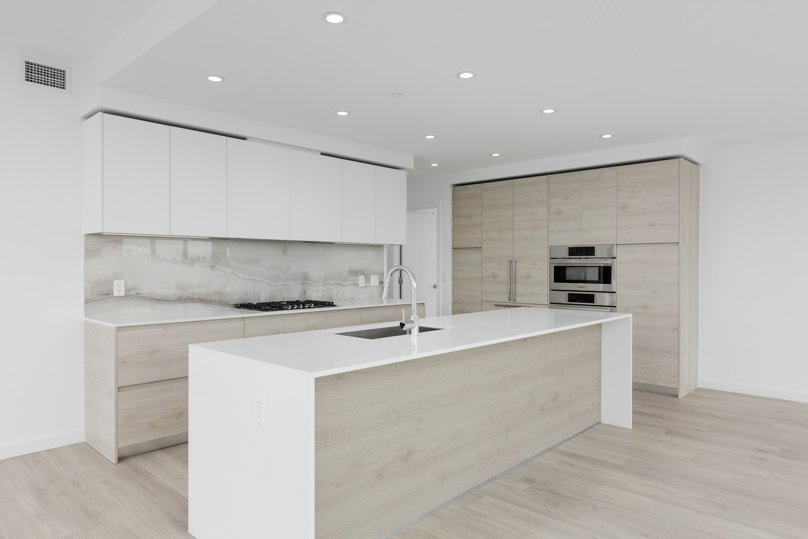 Modern kitchen with white cabinetry, wood accents, and stainless steel appliances. Includes an island with a sink, light wood flooring, and recessed lighting.
