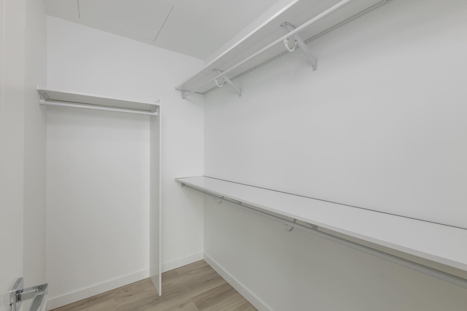Empty white walk-in closet with two long horizontal shelves and hanging racks. Light wood flooring.