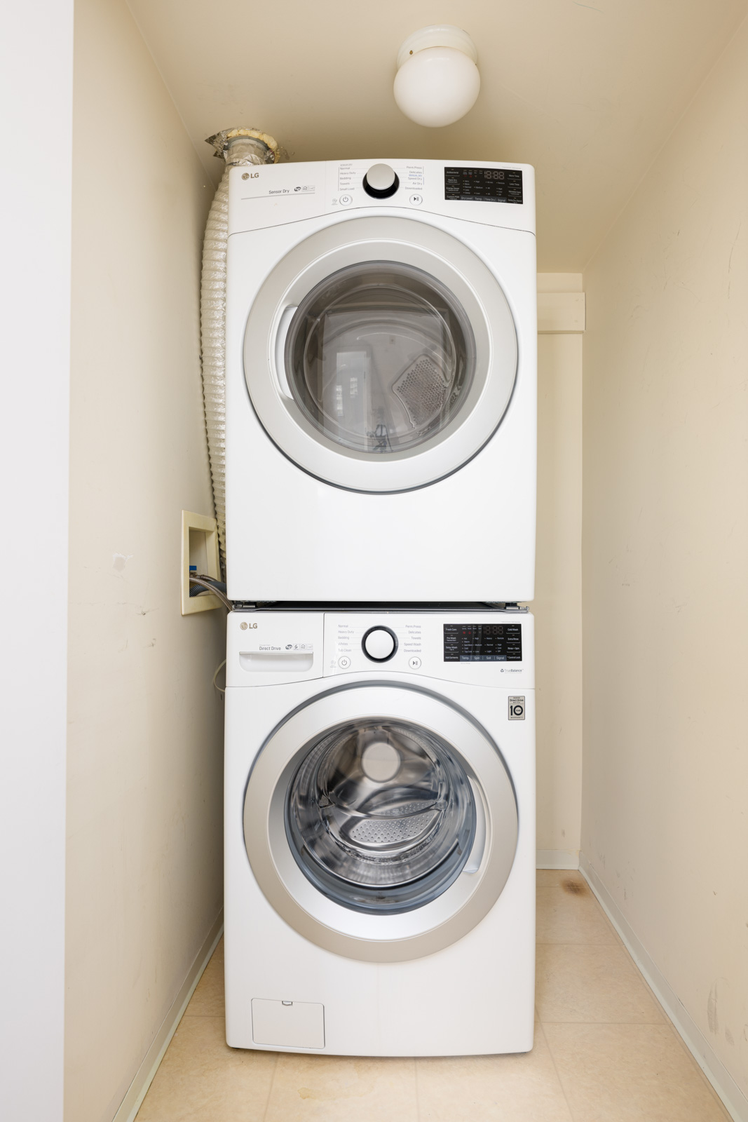 A stacked washer and dryer set is installed in a small laundry nook with beige walls and floor.