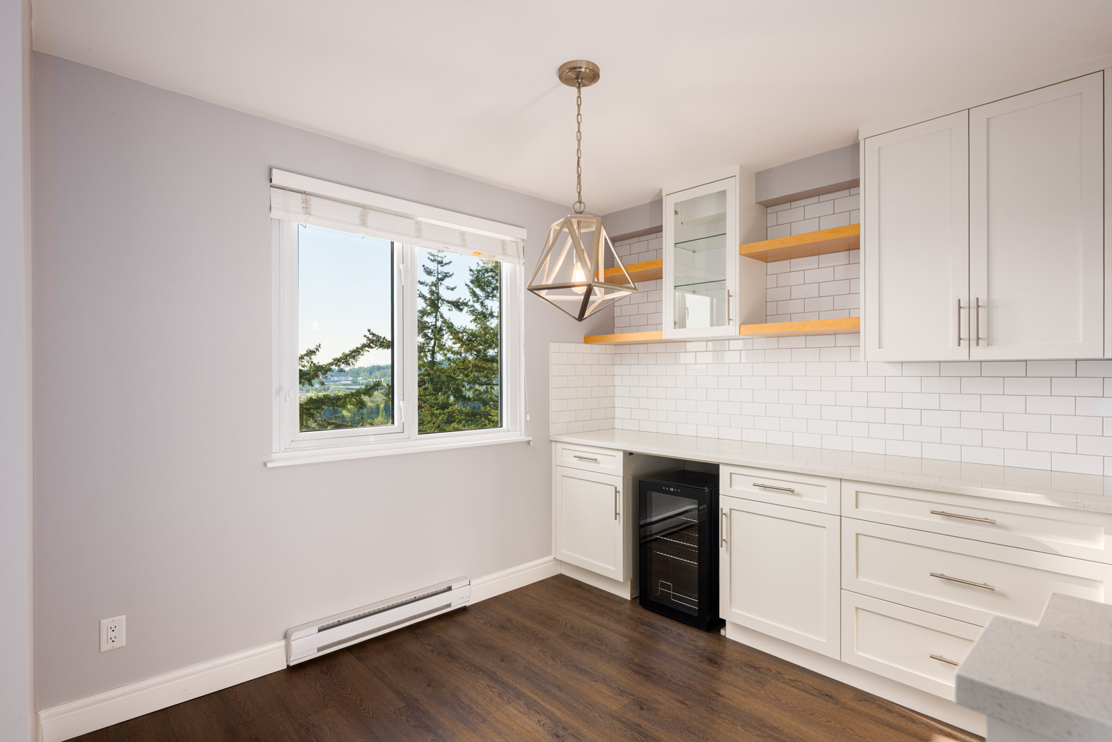 Modern kitchen with white cabinets, subway tile backsplash, wood flooring, a window with a view of trees, pendant light, and built-in wine cooler.