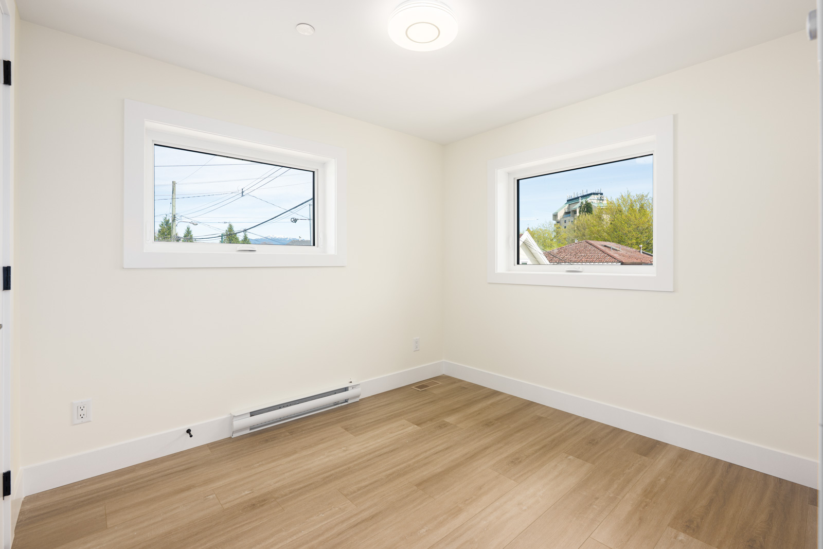 Empty room with light-colored walls, two rectangular windows, wood-look flooring, white baseboard trim, and a ceiling light.