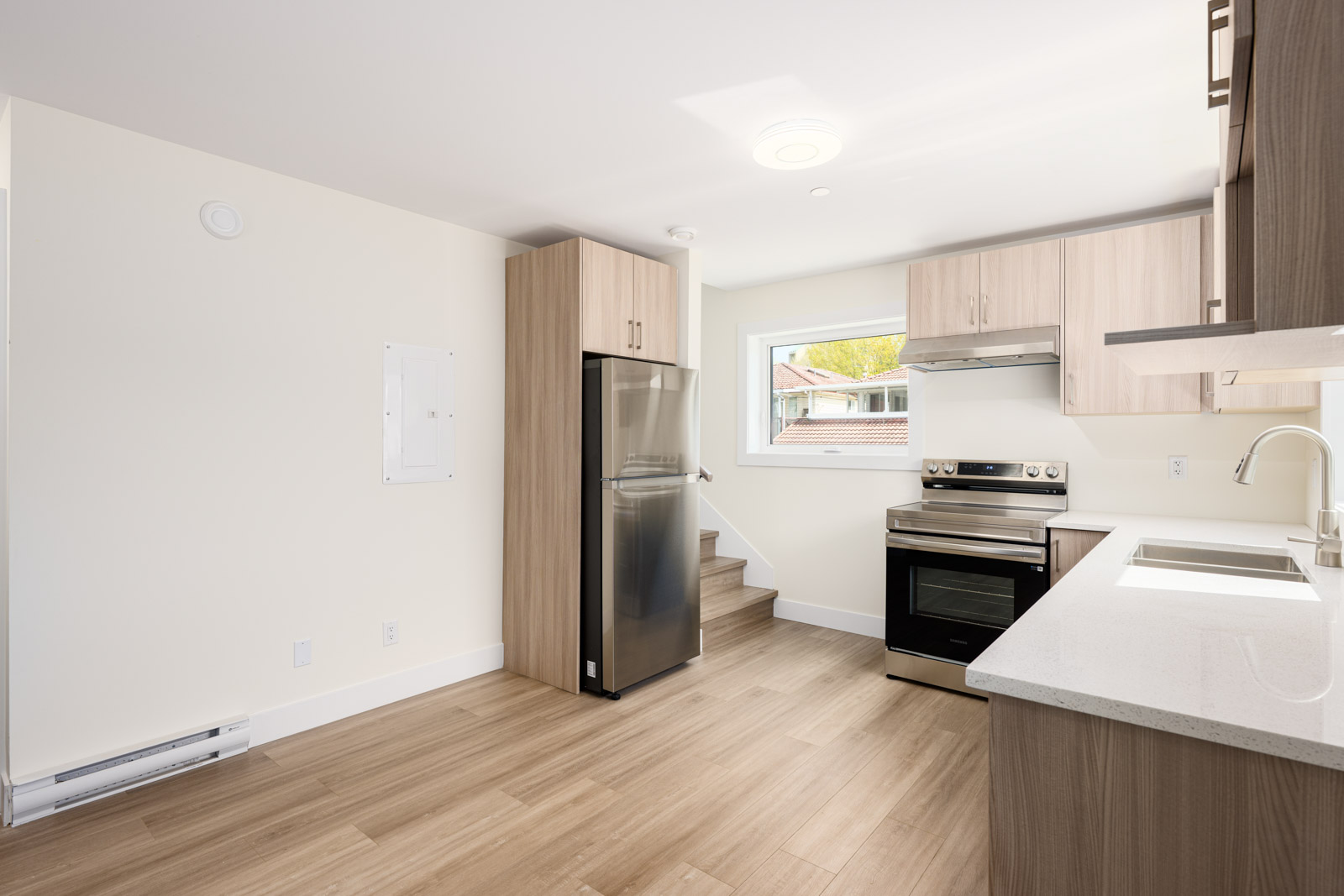 Modern kitchen with light wood cabinets, stainless steel appliances, electric stove, single window, and light wood flooring.