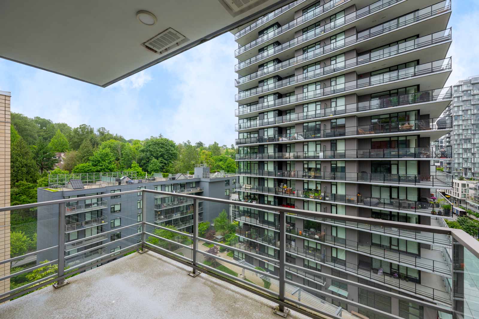 View from a balcony overlooking modern apartment buildings with glass railings and green trees in the background.