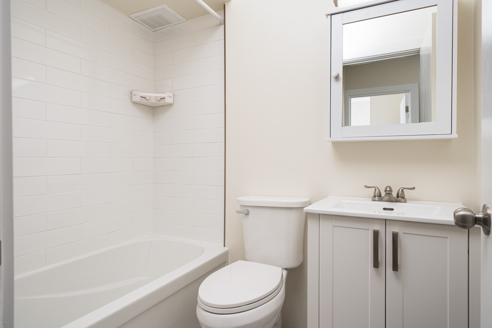 A clean, small bathroom with a white bathtub, toilet, and sink. There's a wall-mounted mirrored cabinet above the sink and neutral-colored walls and tiles.