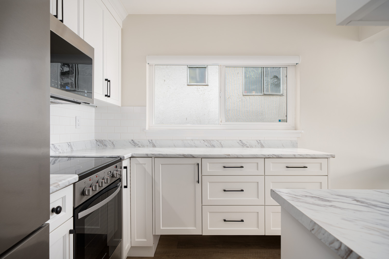 Modern kitchen with white cabinets, a marble countertop, stainless steel appliances, and a large window above the sink.