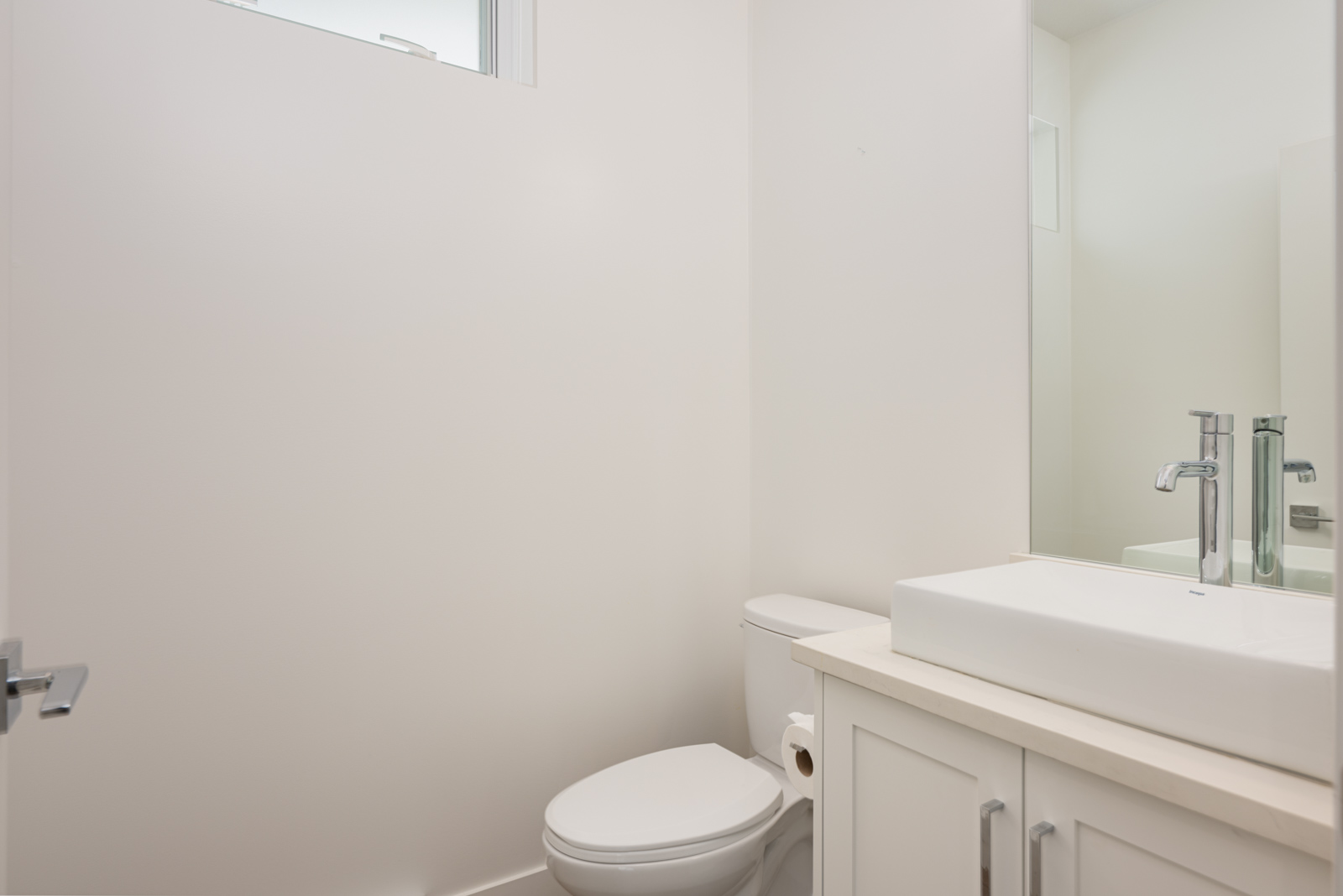 A modern bathroom with a white toilet, a cabinet with a rectangular sink, a silver faucet, and a small window above the toilet.