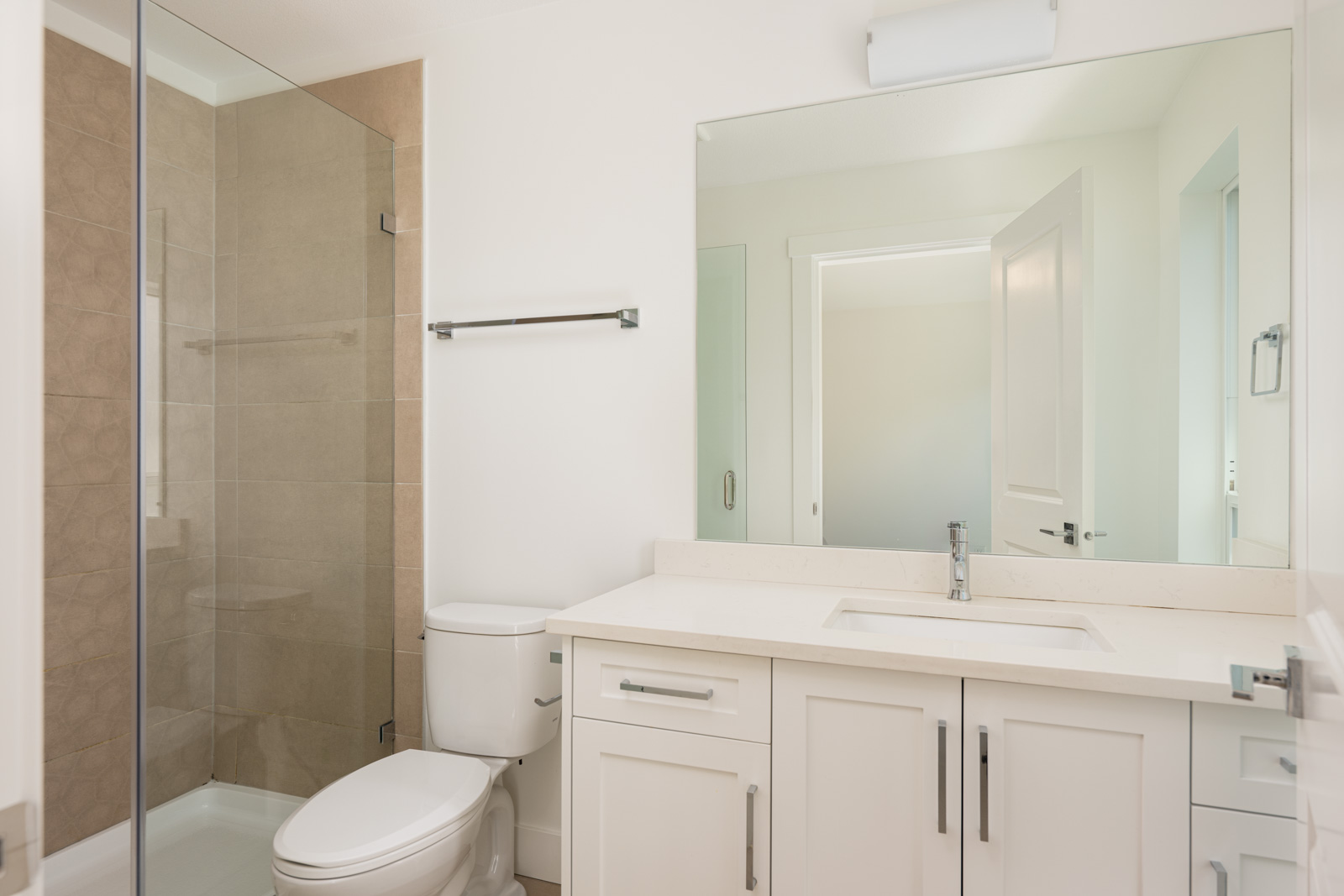 Modern bathroom with a glass-enclosed shower, white vanity with sink, large mirror, toilet, and neutral wall tiles.