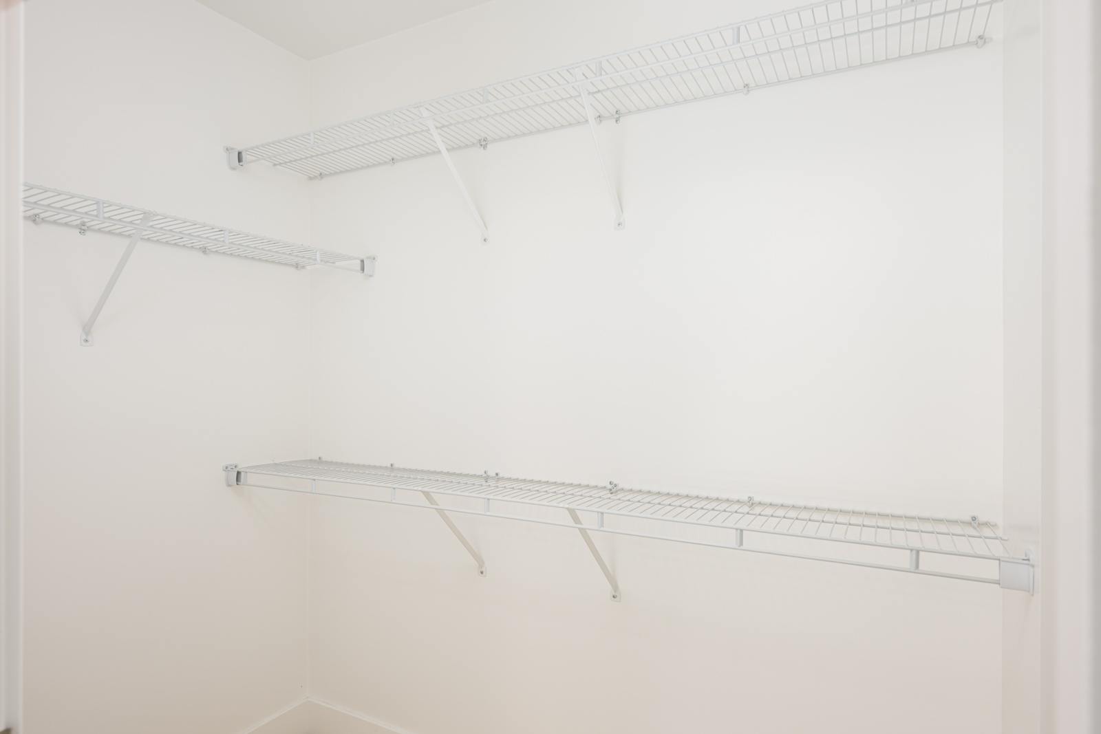 Empty walk-in closet with white walls and three wire shelves mounted on the walls.