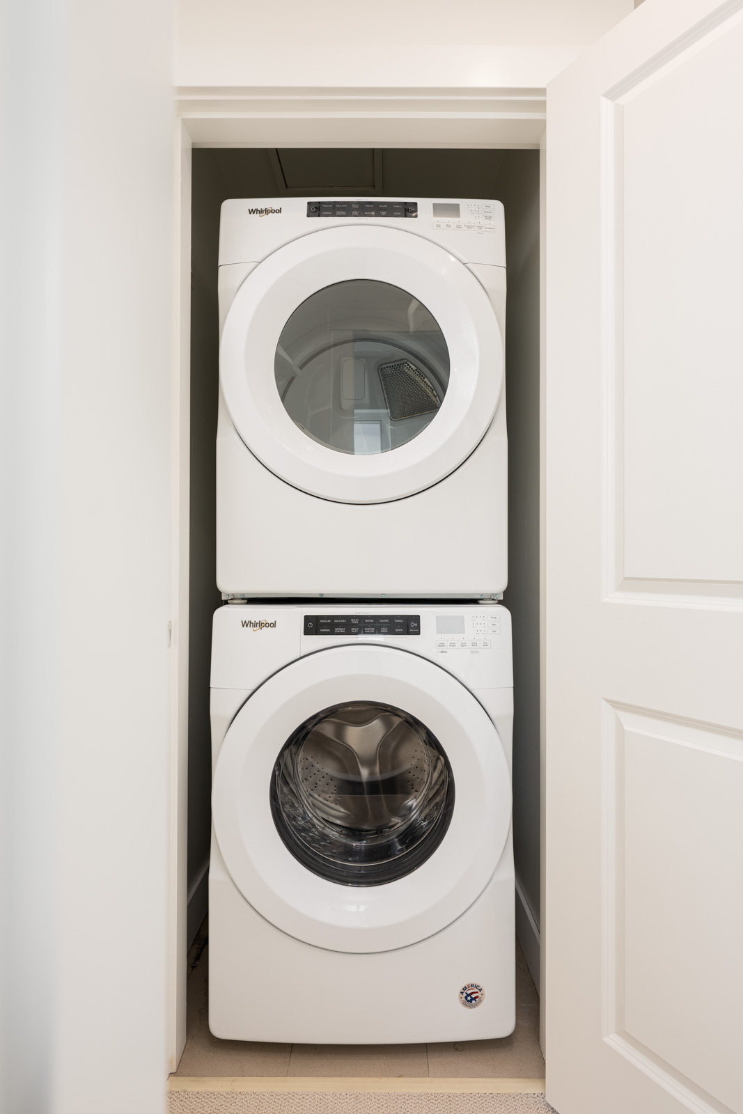 A white stacked washer and dryer set is installed in a small laundry closet with double doors.