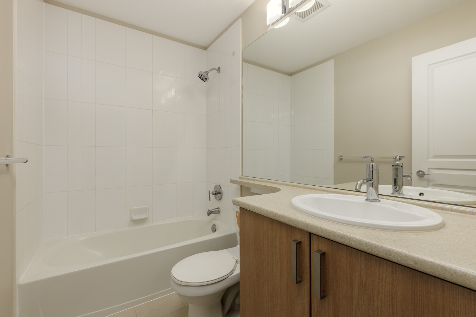 Modern bathroom with a bathtub and shower, toilet, single sink on a beige countertop, large mirror, and wooden cabinetry.