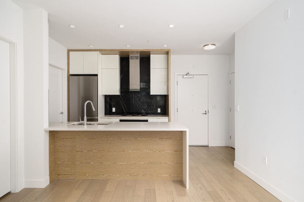 Modern kitchen with a wood island, white countertops, built-in appliances, black backsplash, and light wood flooring in a minimalist open-plan space.