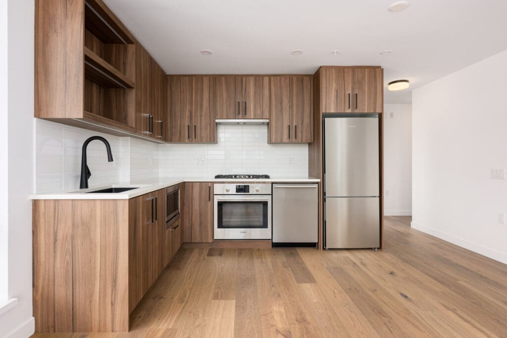 Modern kitchen with wood cabinets, stainless steel appliances, white countertops, and a tile backsplash; includes a built-in oven, gas stove, fridge, dishwasher, and sink with black faucet.