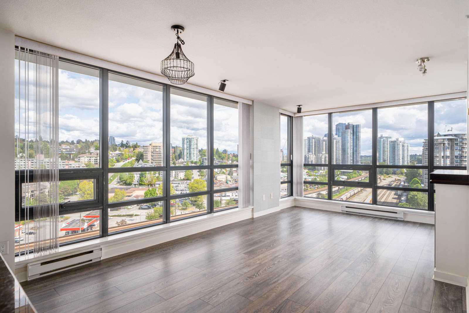 Unfurnished high-rise apartment with floor-to-ceiling windows, wood flooring, and cityscape views under a cloudy sky.