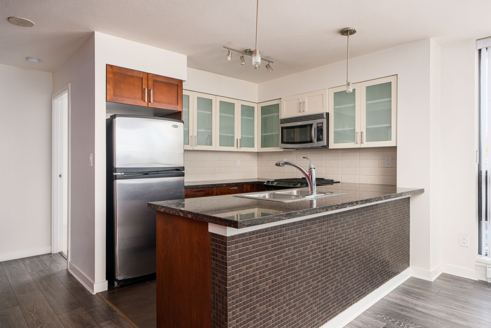 Modern kitchen with stainless steel appliances, glass-front cabinets, dark countertop, tile backsplash, and a central island with a built-in sink.