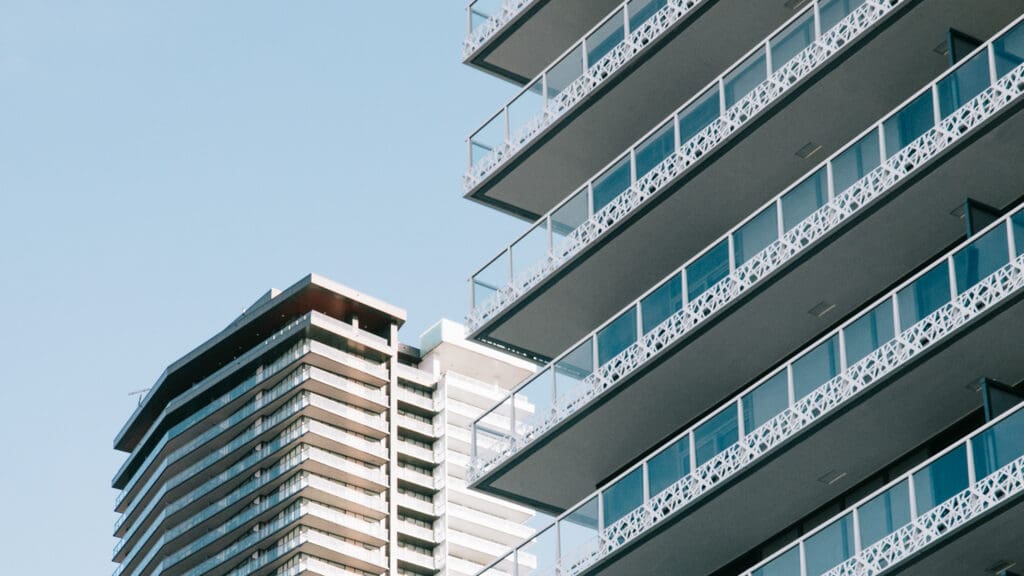 Close-up view of two modern high-rise apartment buildings with balconies against a clear blue sky.