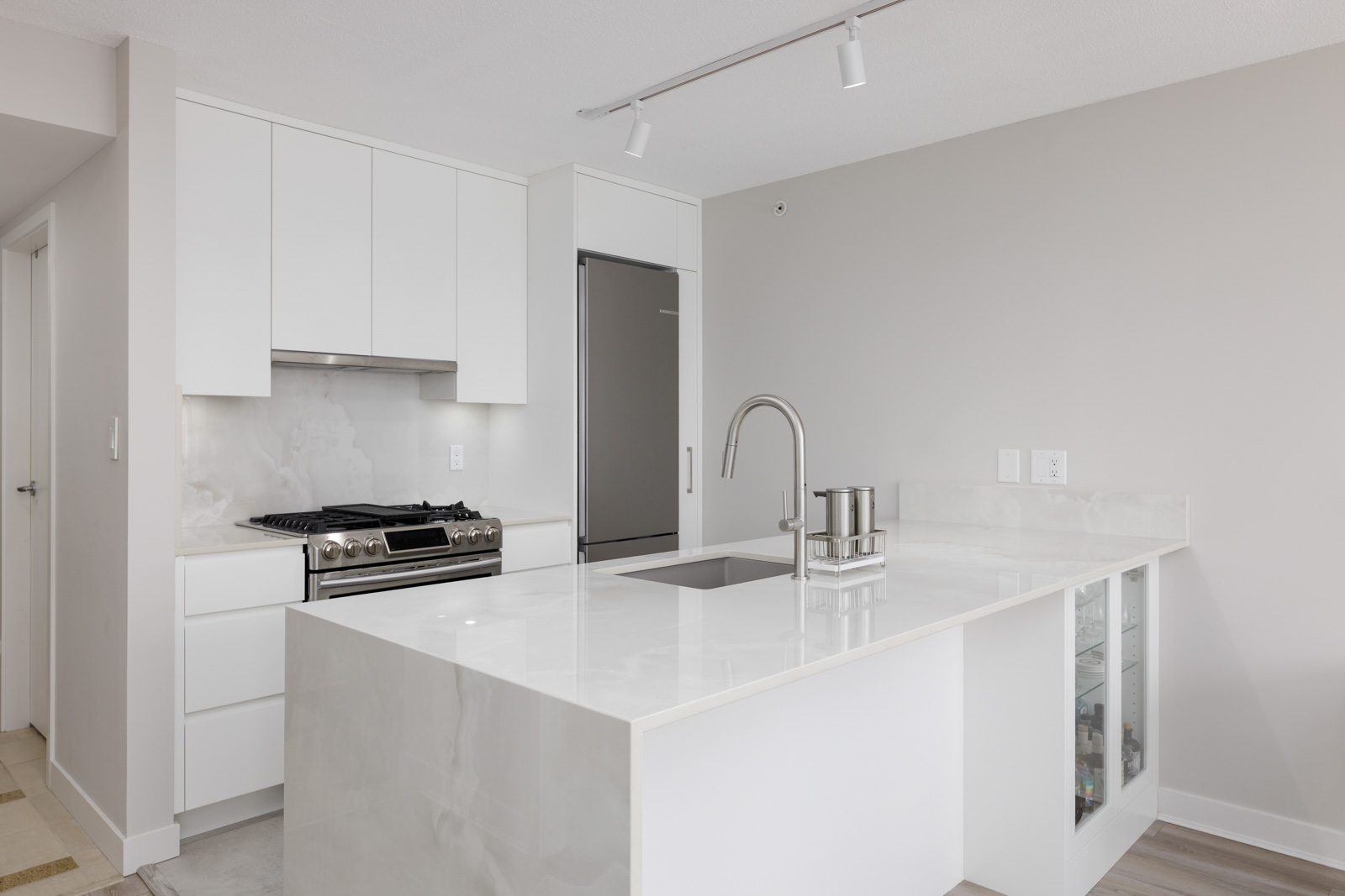 Modern kitchen with white cabinets, stainless steel appliances, a marble island with sink, and glass cabinet doors on the side of the island.