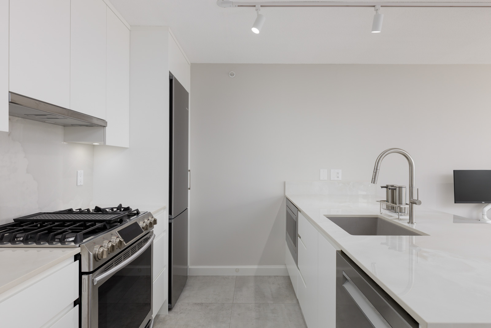 Modern kitchen with white cabinets, stainless steel appliances, gas stove, built-in oven, under-mount sink, faucet, and minimal decor on a clean countertop.