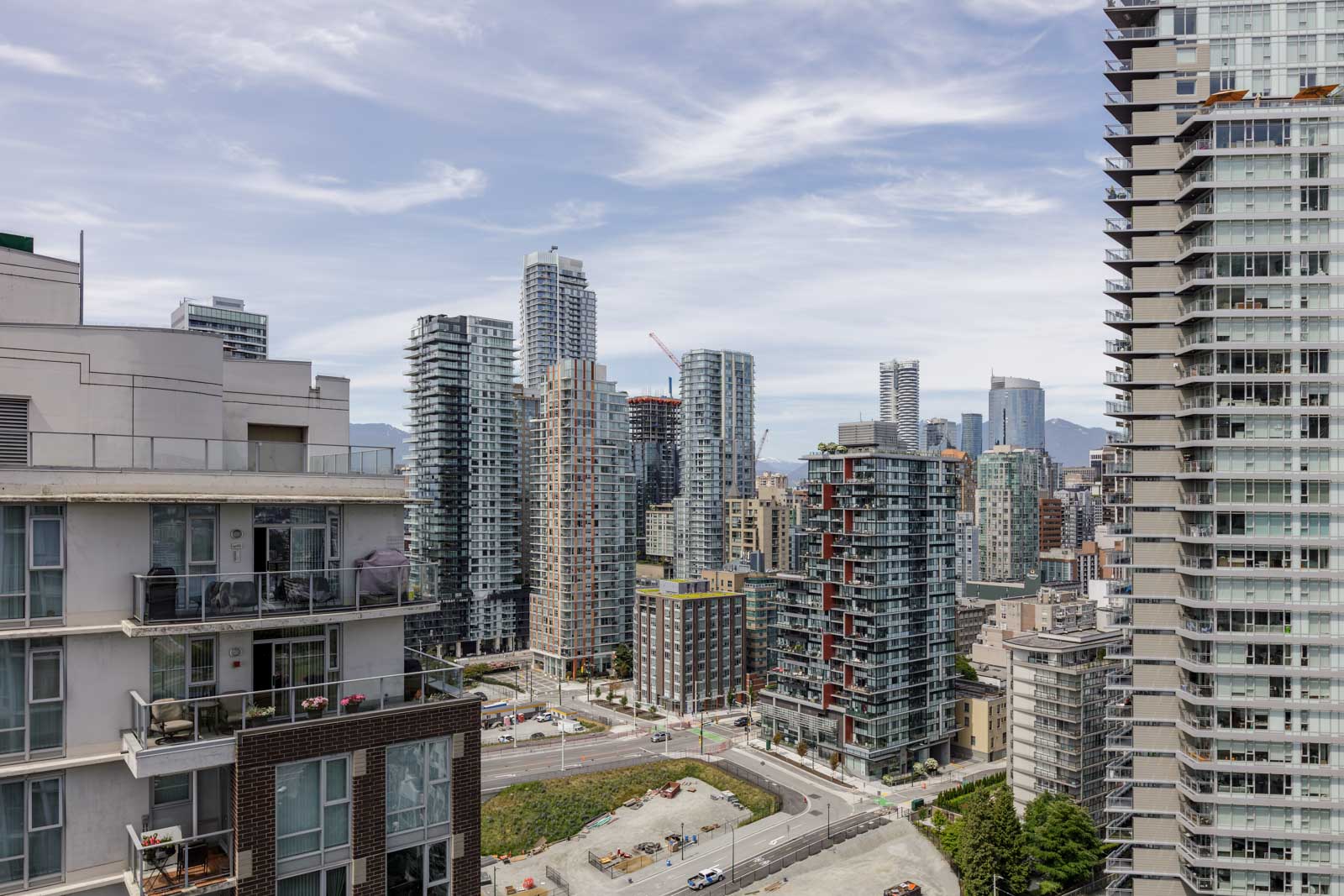 A cityscape with modern high-rise apartment buildings, construction sites, and distant mountains under a partly cloudy sky.