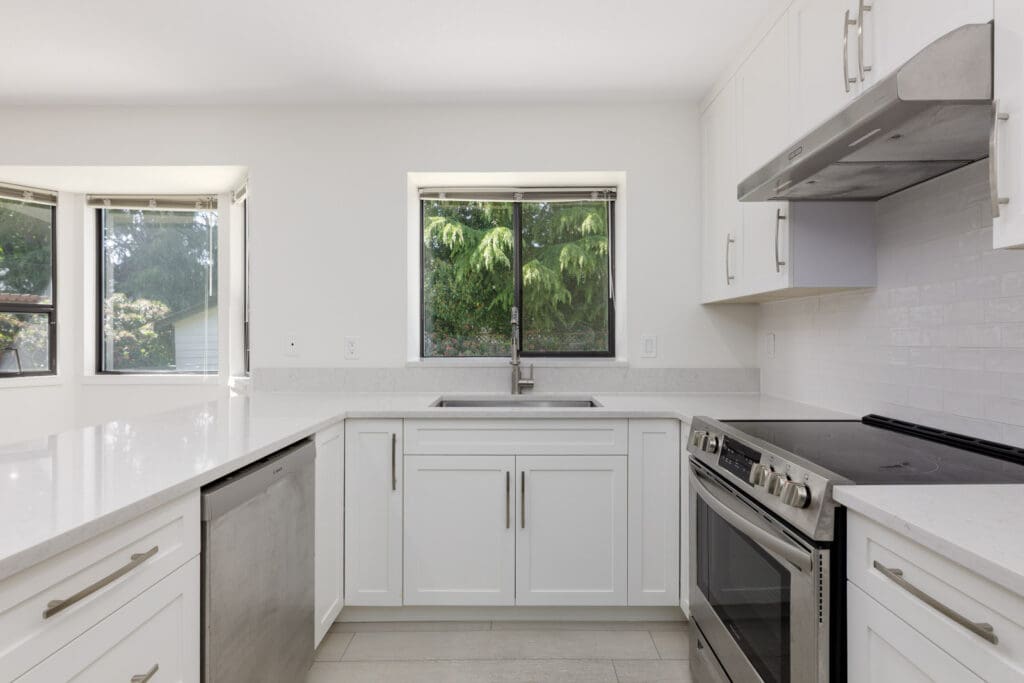 Modern kitchen with white cabinets, stainless steel appliances, and a large window above the sink looking out to greenery.