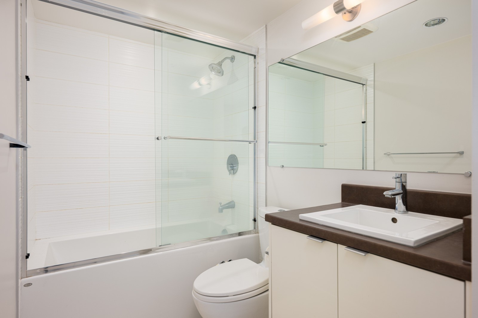 Modern bathroom with a glass-enclosed bathtub and shower, a white sink with a brown countertop, and a large mirror above the vanity.