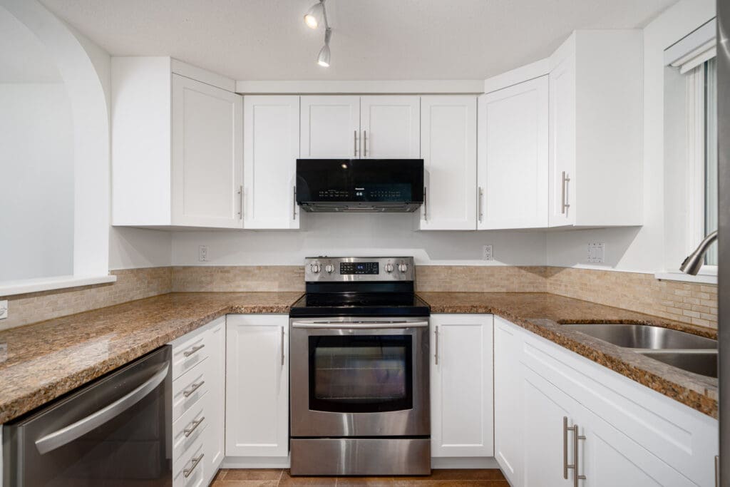 Modern kitchen with white cabinets, stainless steel appliances, granite countertops, under-cabinet range hood, double sink, and neutral backsplash.