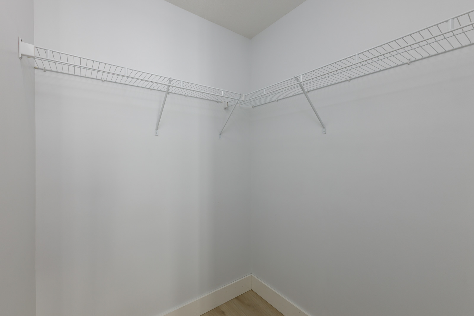 Empty walk-in closet with white walls, light wood floor, and white wire shelving along two walls.