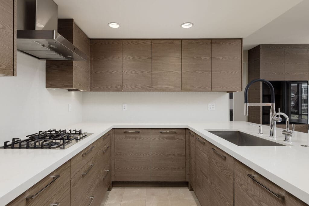 Modern kitchen with wood cabinets, white countertops, gas stove, stainless steel range hood, and a sink with a high-arc faucet.