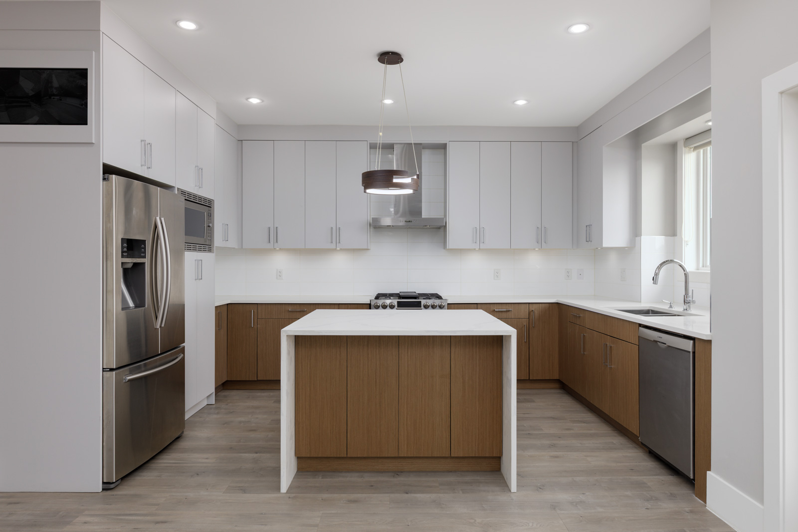 Modern kitchen with stainless steel appliances, a central island, white upper cabinets, wooden lower cabinets, and light wood flooring.