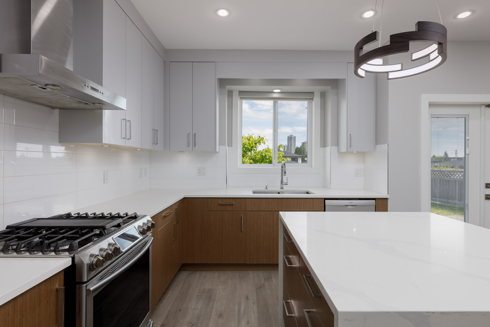 Modern kitchen with white countertops, stainless steel appliances, wood cabinetry, a central island, and a window above the sink letting in natural light.