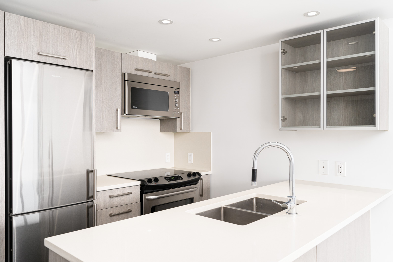 Modern kitchen with light wood cabinets, stainless steel appliances, an island with a sink, and an open glass-front cabinet.