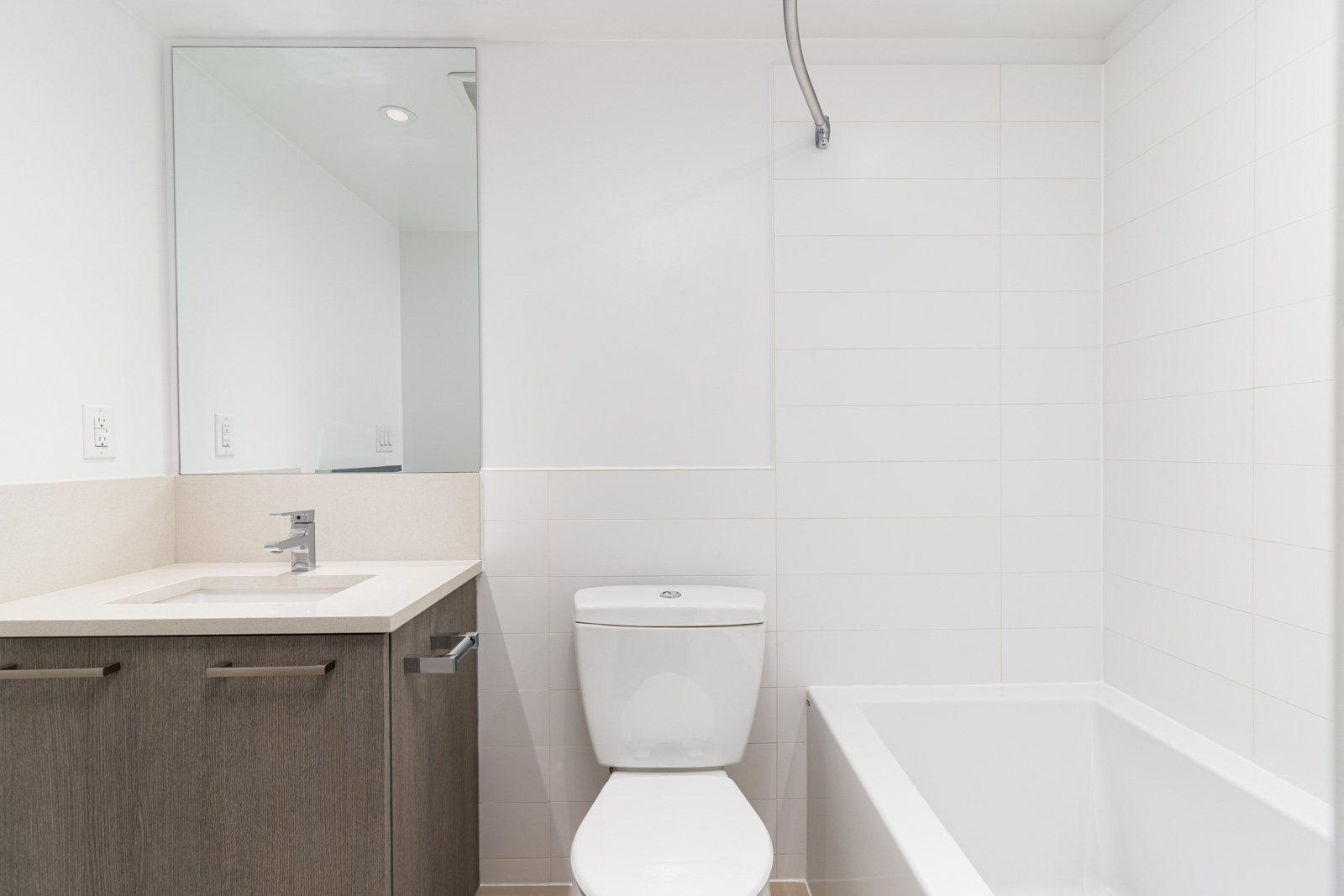 A modern bathroom with a sink and cabinet on the left, a toilet in the center, and a bathtub on the right, all with white tiles and walls.