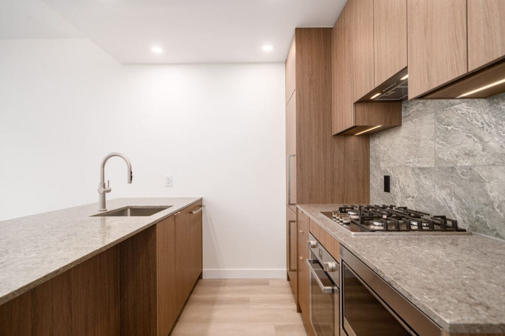 Modern kitchen with wood cabinets, marble countertops, built-in oven, gas cooktop, integrated sink, and minimalist design under recessed ceiling lights.