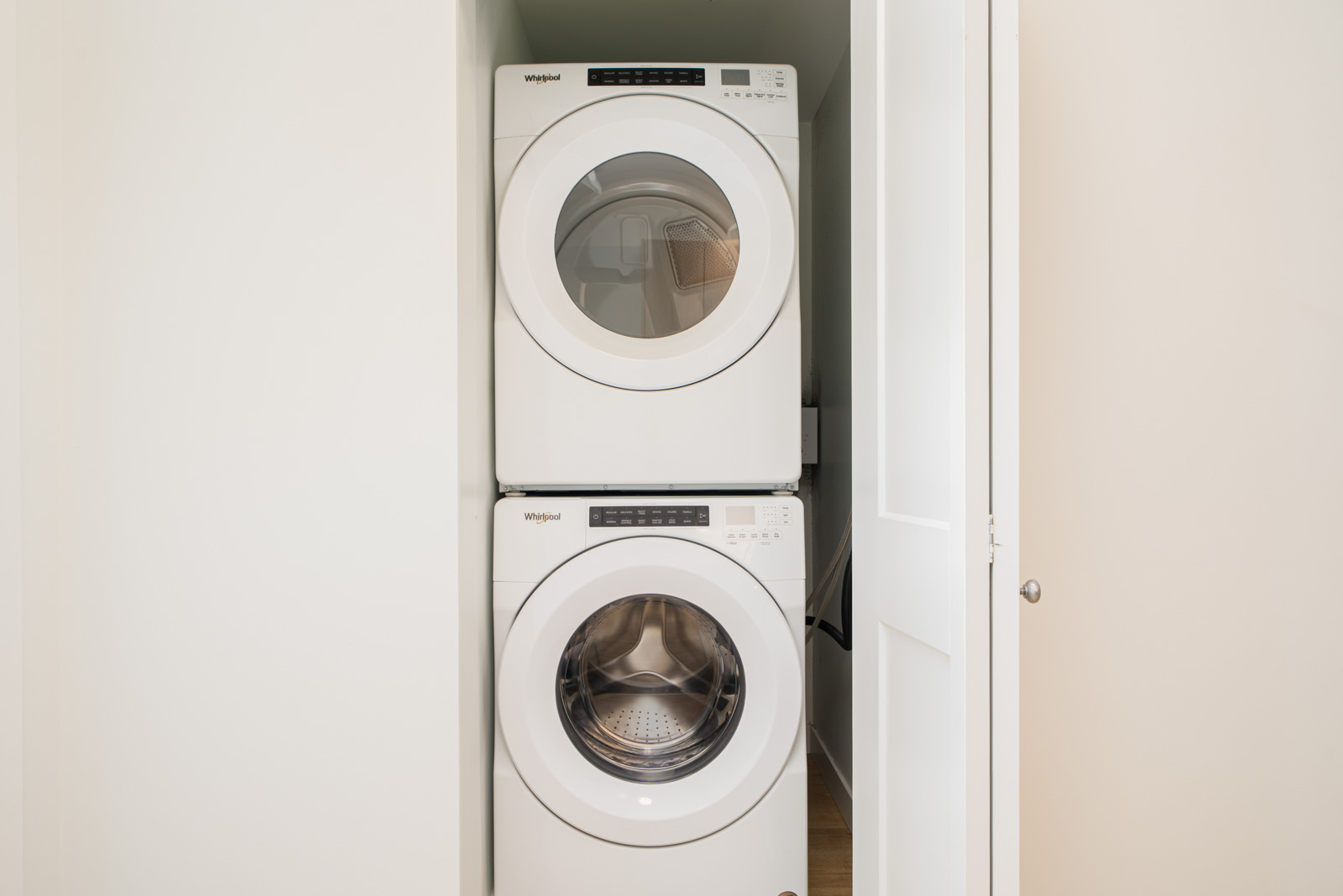 A stacked washer and dryer unit is installed in a small closet with the door partially open.