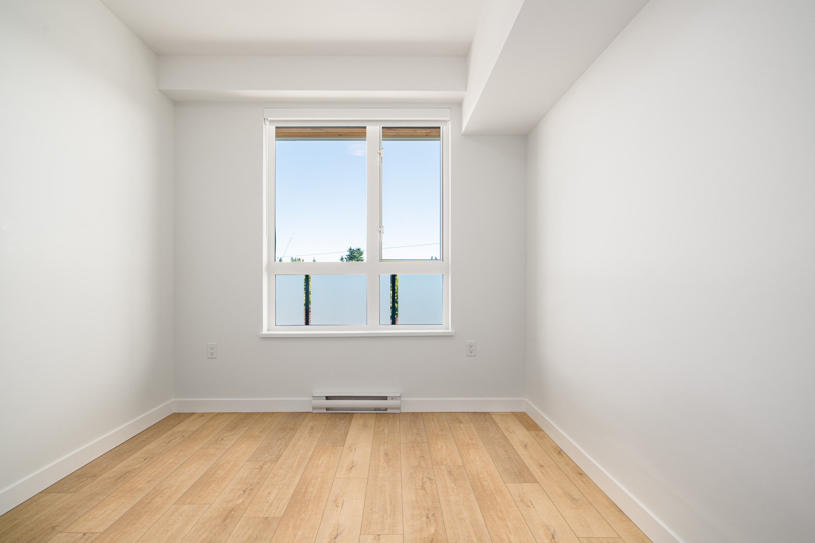 Empty room with light-colored wooden flooring, white walls, a large window, and a baseboard heater beneath the window.