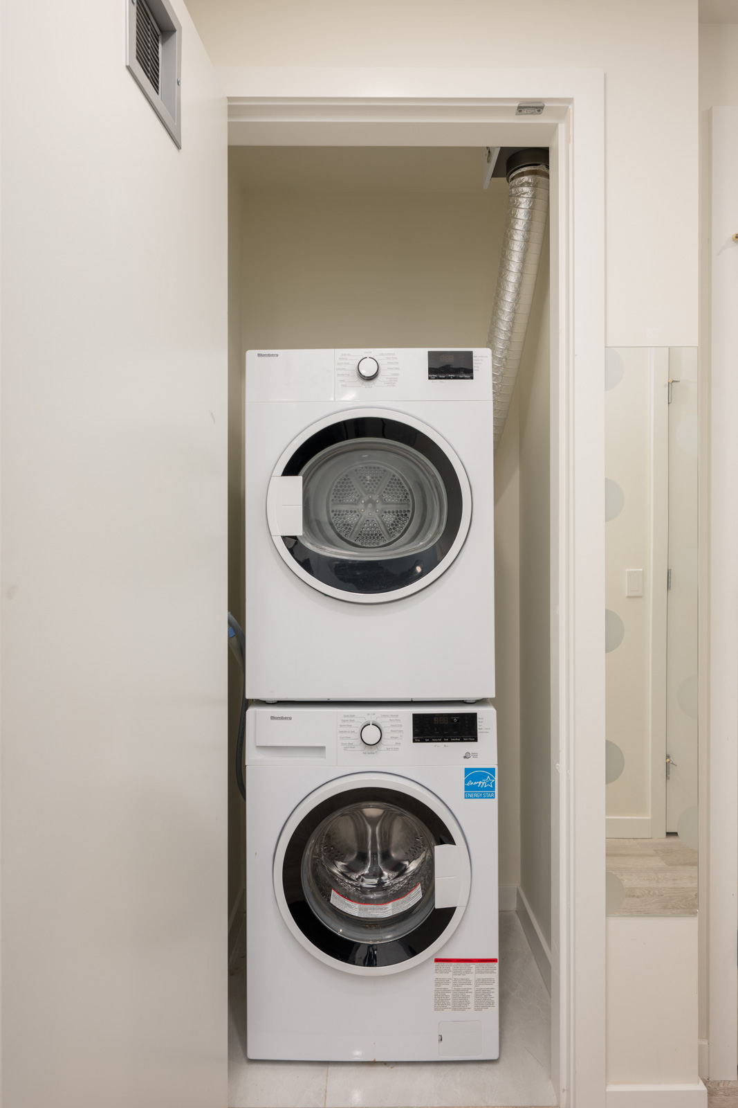 A stacked washer and dryer are installed in a small laundry closet with a vent pipe connected to the dryer.