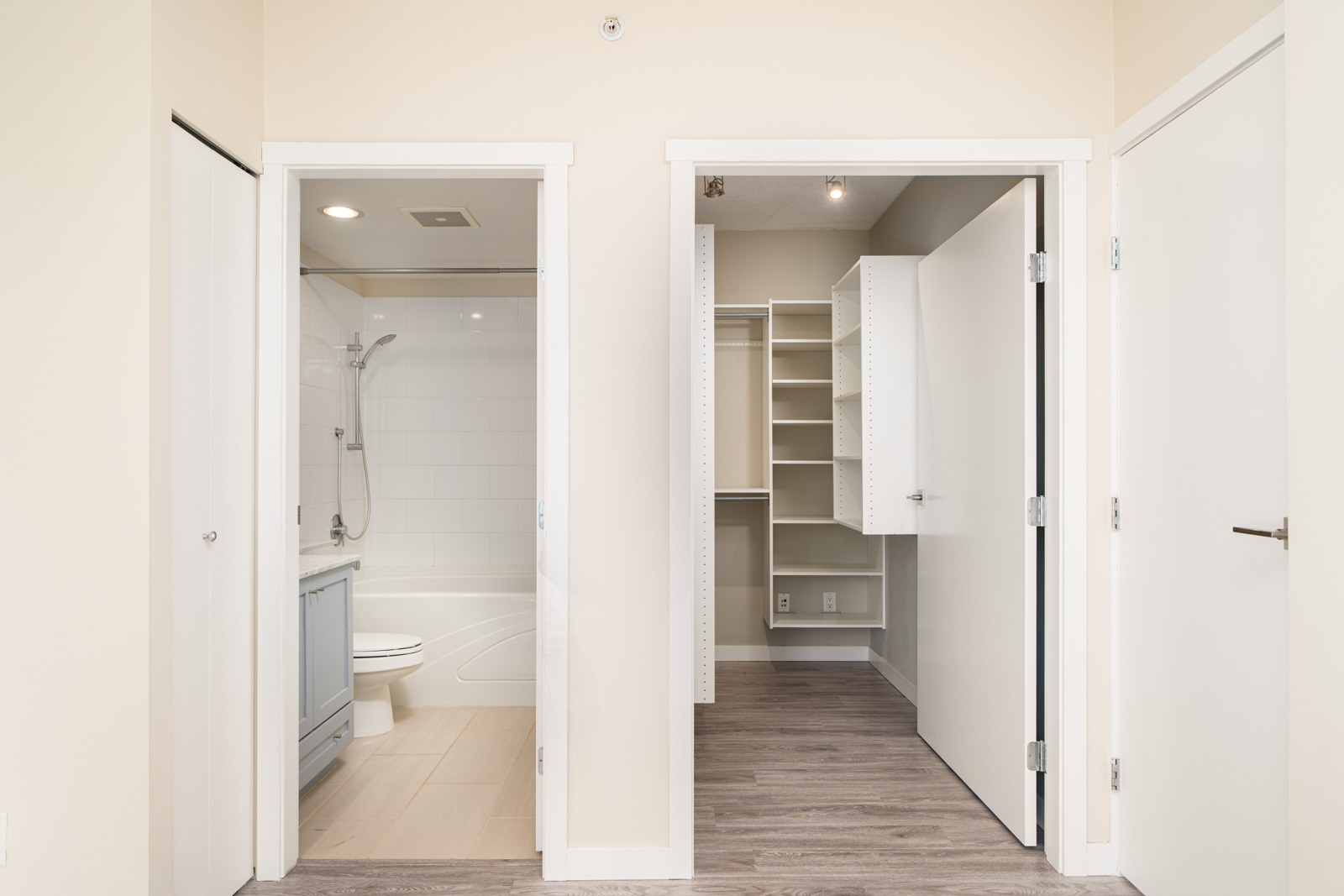 A bathroom with a bathtub and shower is on the left, and an empty walk-in closet with shelving is on the right, both with open white doors.