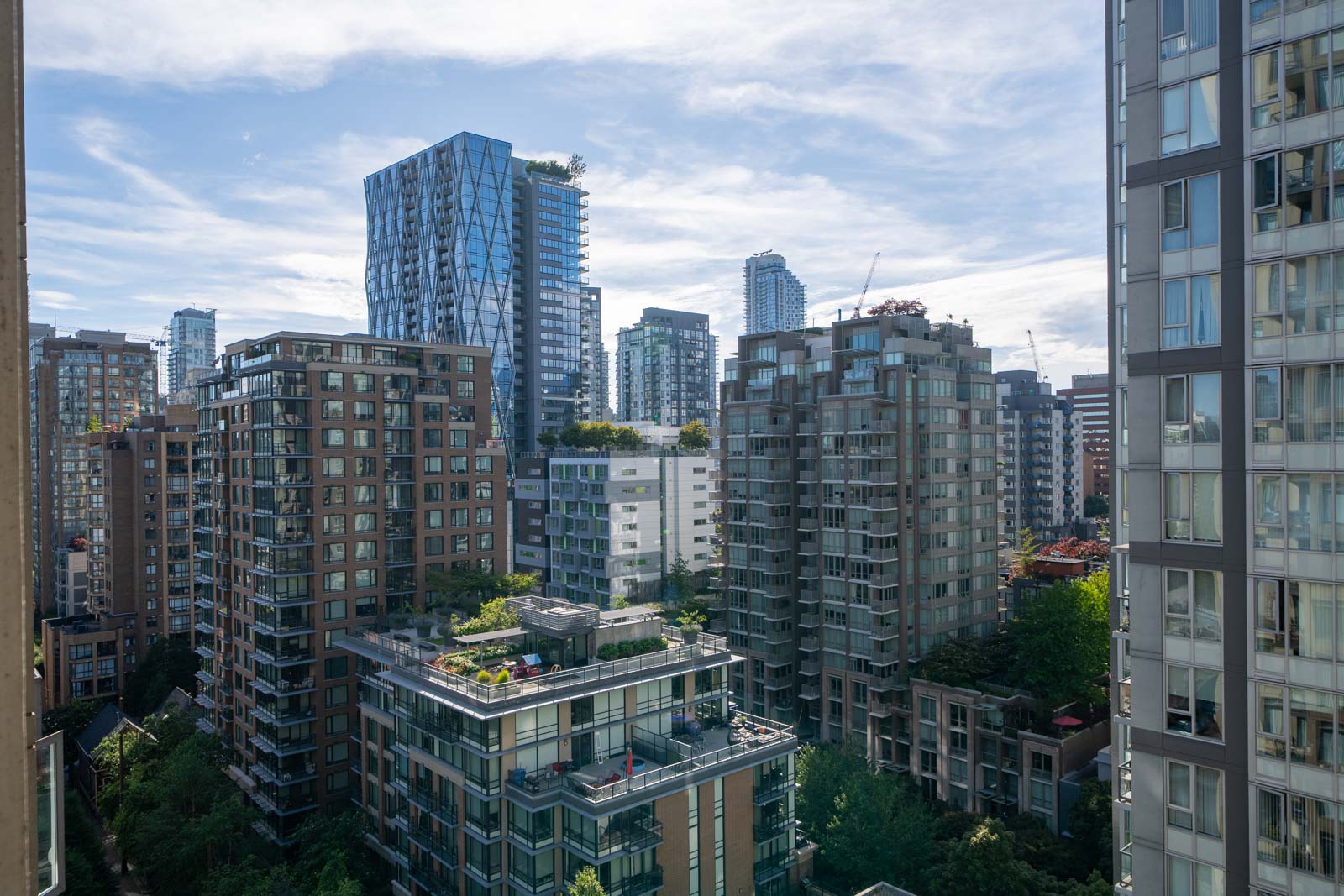 High-rise apartment and condo buildings in a cityscape with greenery and trees visible on rooftops and ground level under a partly cloudy sky.