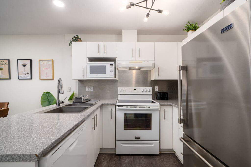 Modern kitchen with white cabinets, stainless steel appliances, a double sink, electric stove, microwave, and wall art in the background.