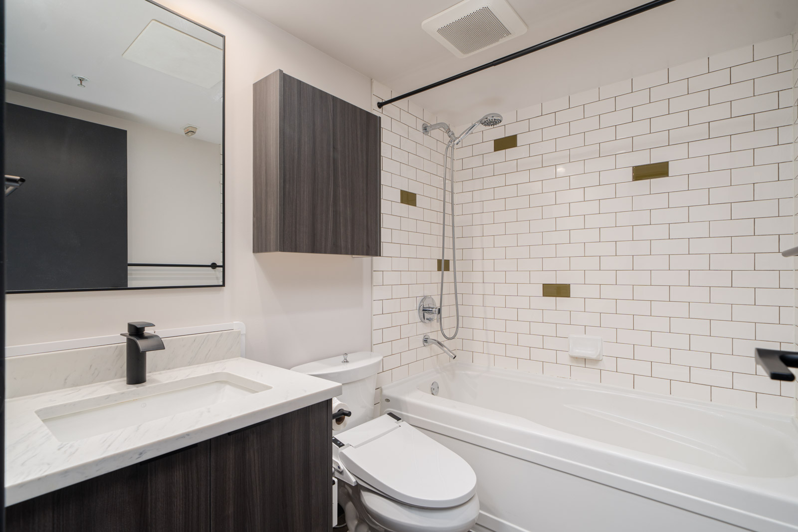 Modern bathroom with a white bathtub, wall-mounted shower, subway tile wall with accent tiles, a sink with marble countertop, dark cabinetry, and a large mirror.