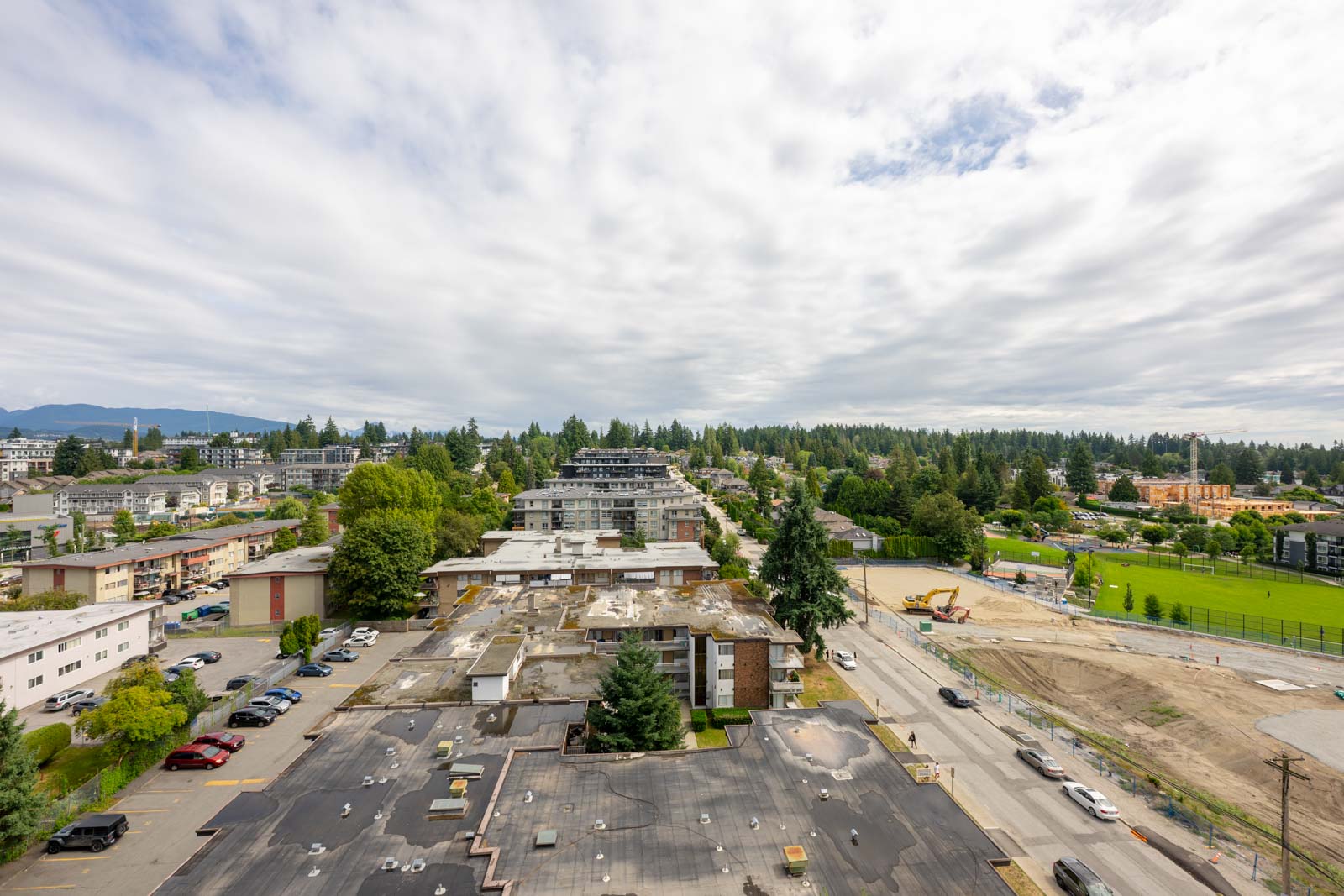 Aerial view of a suburban neighborhood with apartment buildings, trees, a construction site, and a cloudy sky overhead.
