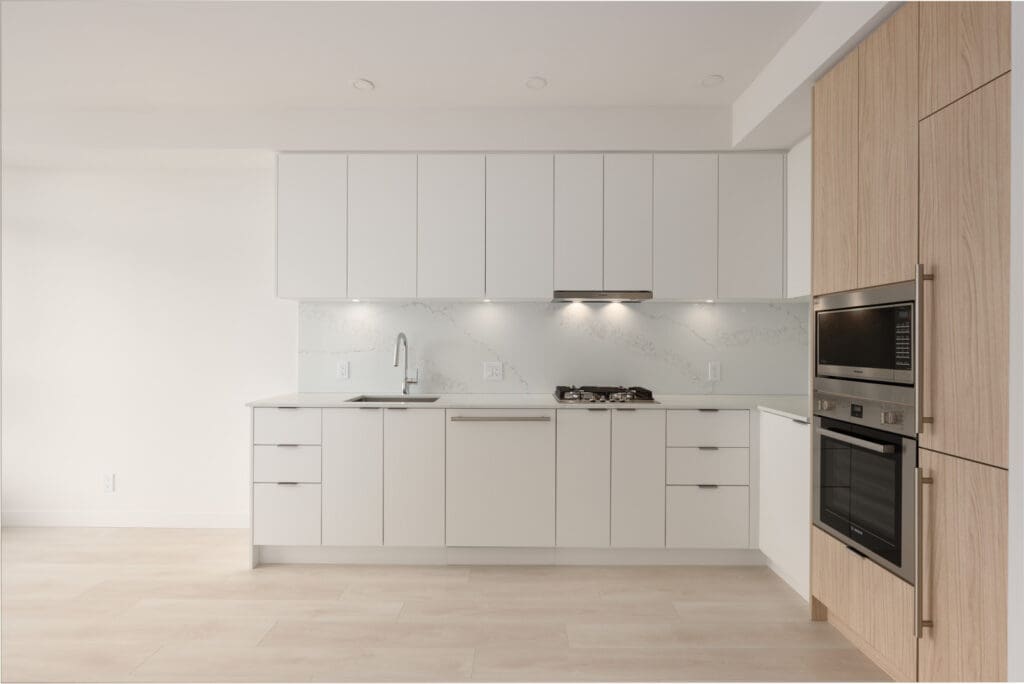 Modern kitchen with white cabinets, built-in oven and microwave, gas stove, sink, and light wood accents. The space is clean, minimalistic, and well-lit.