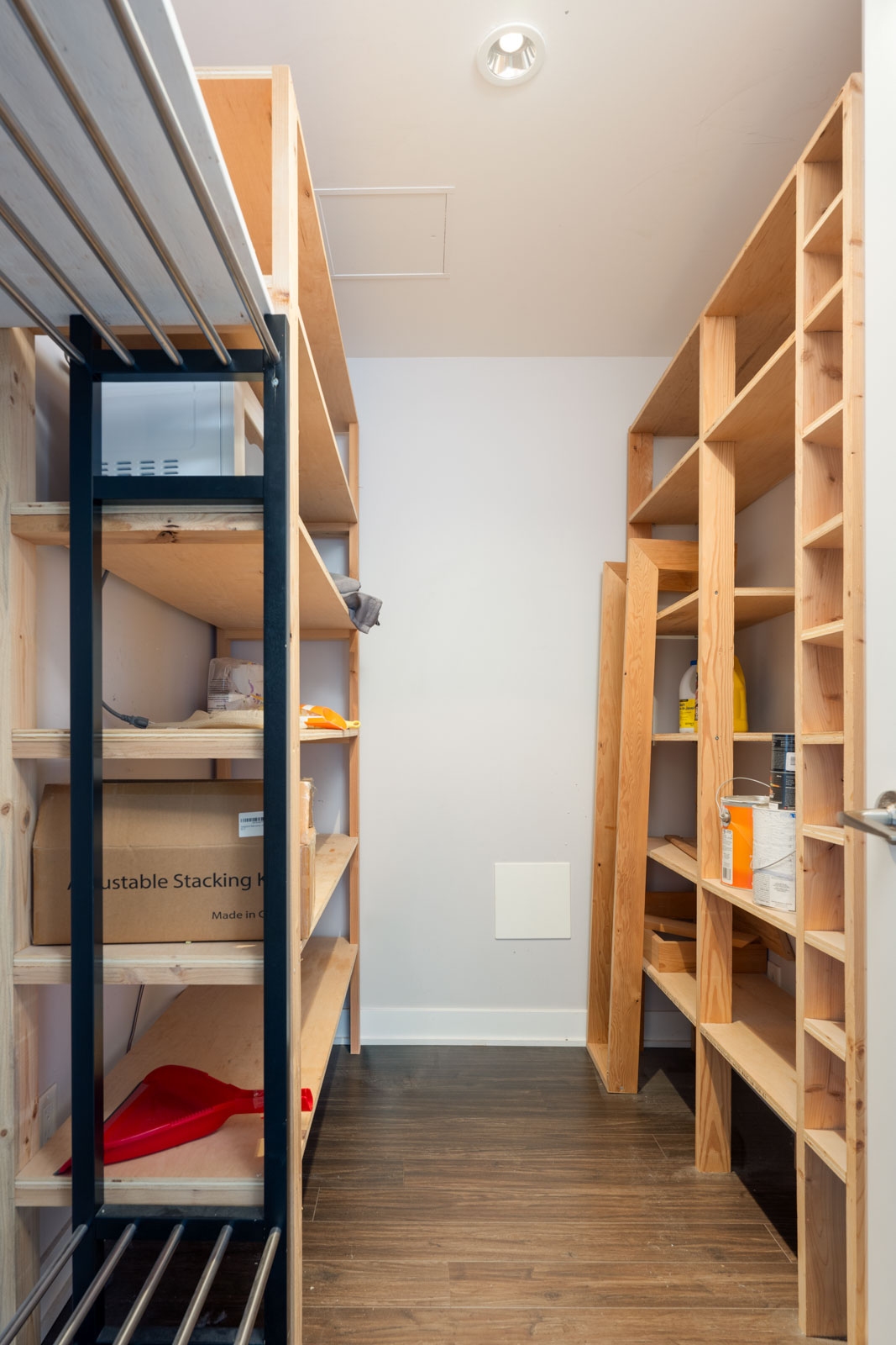 A storage room with wooden shelves on both sides, containing boxes and various items, and a wood floor.