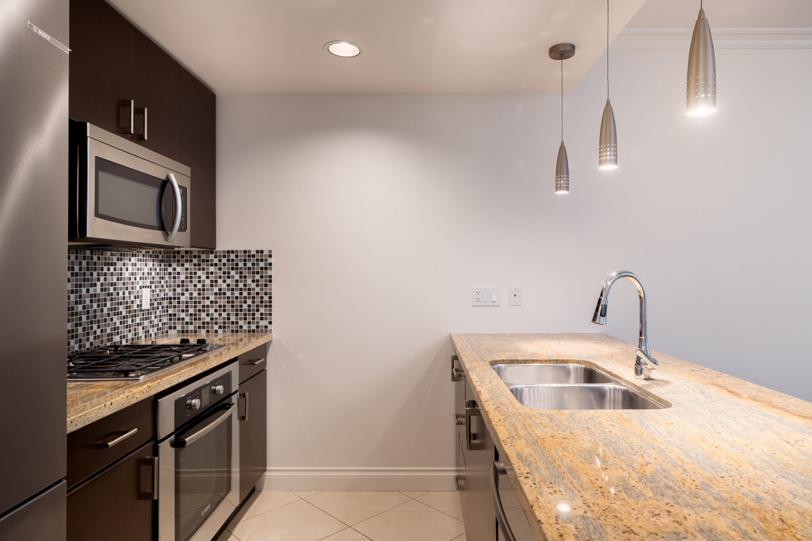 Modern kitchen with stainless steel appliances, mosaic tile backsplash, granite countertops, double sink, and pendant lighting.