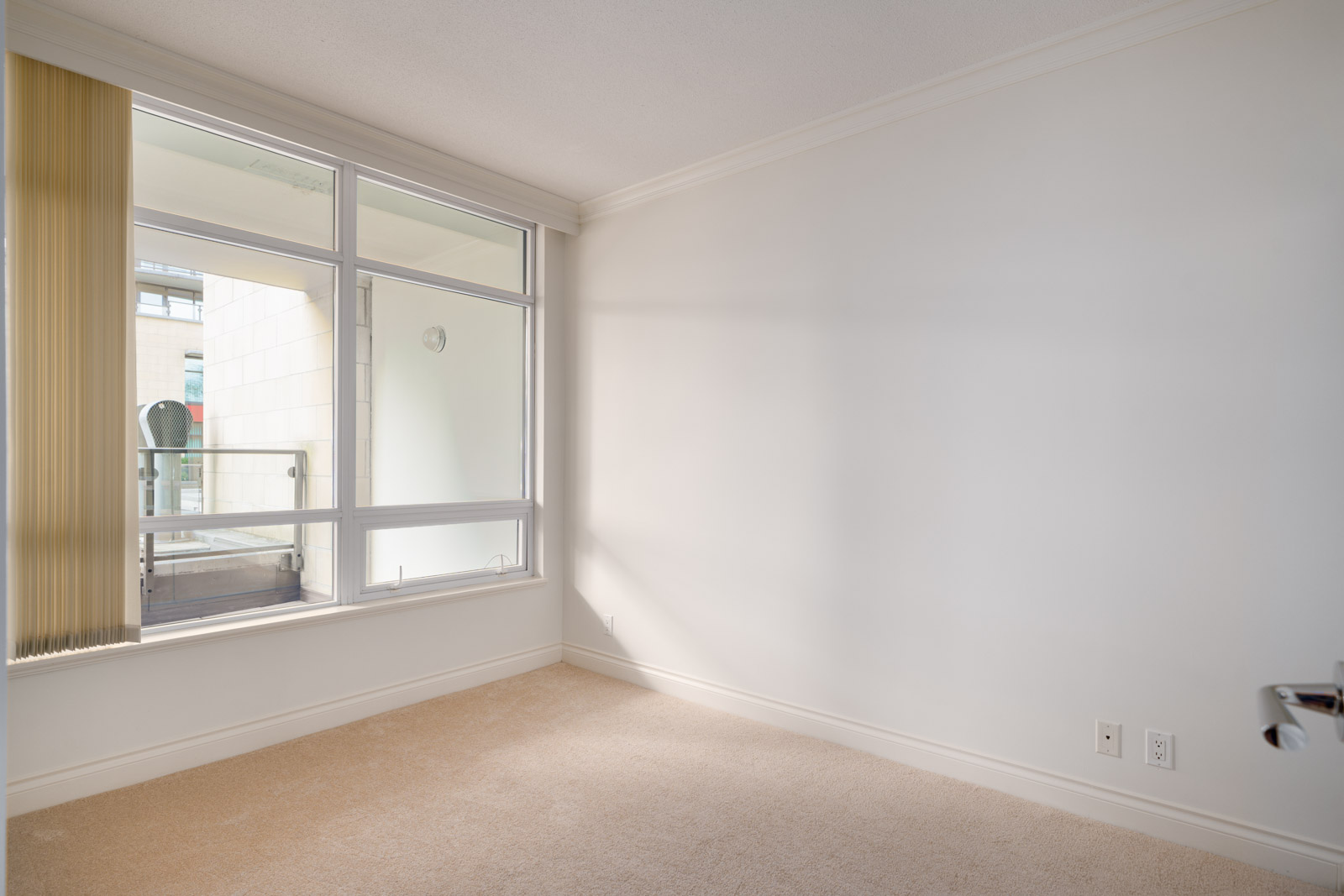 Empty room with beige carpet, white walls, and a large window with vertical blinds letting in natural light.