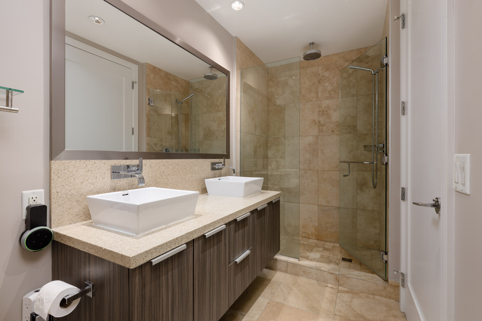 Modern bathroom with a double vanity, two square sinks, large mirror, and a glass-enclosed walk-in shower with beige tiles.